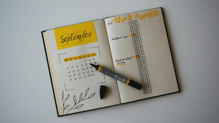 Agenda abierta con un calendario mensual y recordatorios escritos junto a un rotulador amarillo